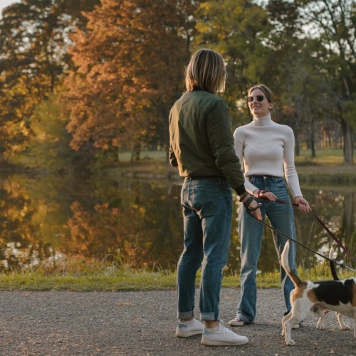Two people walking dogs by a lake