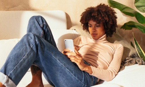 a person laying down looking at a phone with a plant behind them